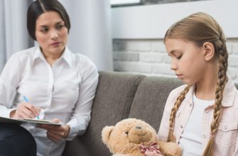 Therapist sitting with a clipboard talking to a girl on a couch, holding a blue pen for notes