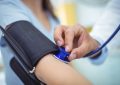 Close-up of a clinician inflating a blue blood pressure cuff around a patient’s upper arm during a checkup.