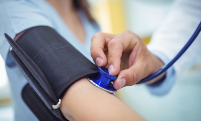Close-up of a clinician inflating a blue blood pressure cuff around a patient’s upper arm during a checkup.