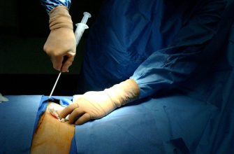 Surgeon in blue scrubs and mask performing leg surgery with an visible incision.