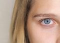 Close-up of a blue eye with long lashes and light skin, hair framing the left side of the image.