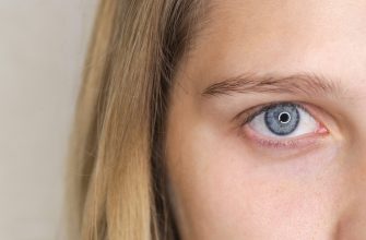 Close-up of a blue eye with long lashes and light skin, hair framing the left side of the image.