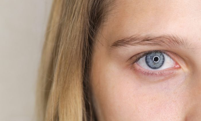 Close-up of a blue eye with long lashes and light skin, hair framing the left side of the image.