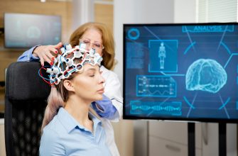Researcher adjusts an EEG cap on a woman during brain-monitoring, with a blue digital 'analysis' display in the background.