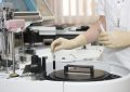 Laboratory technician in gloves placing a small test vial into an automated analyzer.