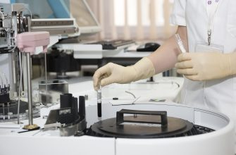 Laboratory technician in gloves placing a small test vial into an automated analyzer.