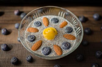 Chia pudding in a glass bowl with blueberries and almonds on a wooden table, with a yellow garnish on top