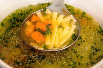 Ladle scooping light broth with white asparagus, carrot chunks, and chopped herbs in a pot.