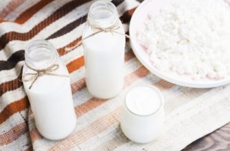 Glass milk bottles tied with twine resting on a striped cloth with a bowl of cottage cheese nearby in a rustic setting.