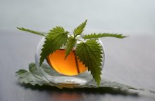 Nettle leaves arranged across a transparent glass with an amber drink inside, resting on a reflective surface.
