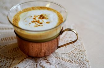 Latte or cappuccino in a glass mug with frothy milk on a lace tablecloth.