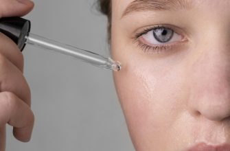 Close-up of a hand using a dropper to apply skincare serum to the cheek on a person's face
