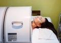 Person undergoing an MRI scan with their head inside the scanner, resting on a pillow and covered with a white gown/blanket.