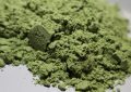 Close-up of a mound of green powder with a fine, crumbly texture on a white surface.