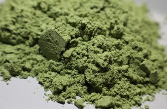 Close-up of a mound of green powder with a fine, crumbly texture on a white surface.